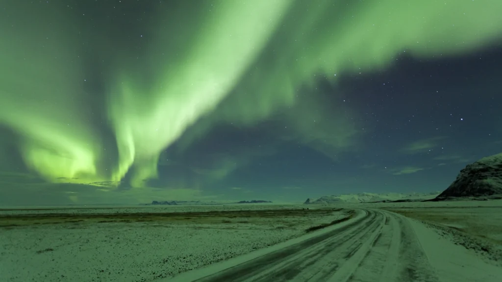 Auroras boreales sobre una carretera nevada en Islandia, cielo estrellado