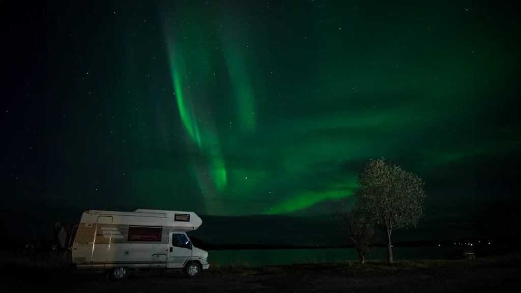 Camper estacionada bajo auroras boreales en Islandia, noche estrellada