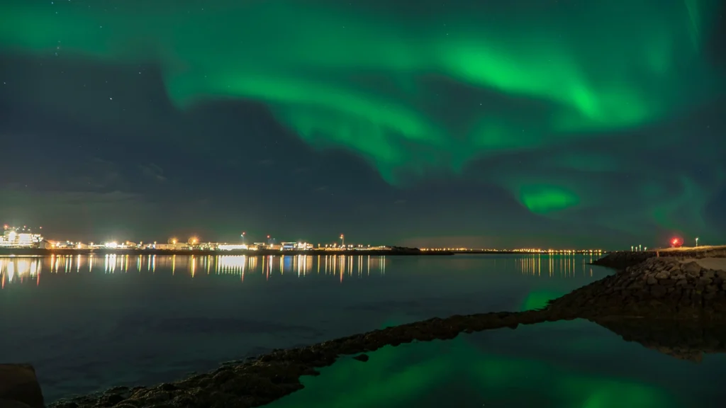 Auroras boreales sobre Reikiavik con reflejo en el agua, Islandia