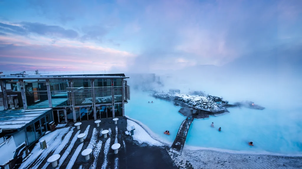 Blue Lagoon en Islandia con vapor geotérmico, pasarela de madera y bañistas al atardecer en invierno