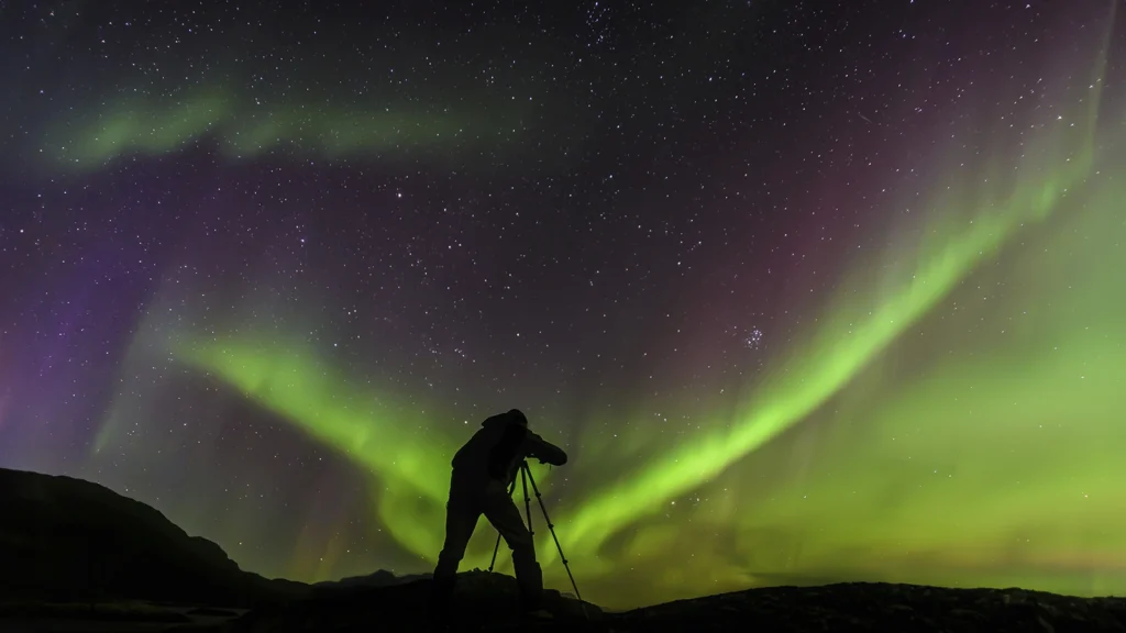 Fotógrafo con trípode capturando auroras boreales bajo cielo estrellado en Islandia