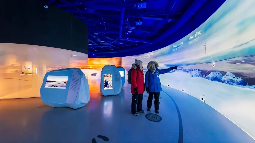 Dos visitantes en la exposición “Wonders of Iceland” de Perlan en Reikiavik, frente al panel sobre glaciares (jökulhlaup)