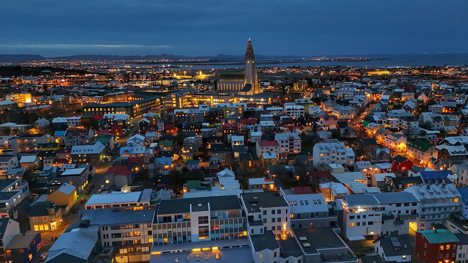 Vista aérea de Reikiavik al anochecer con Hallgrímskirkja iluminada y la bahía al fondo