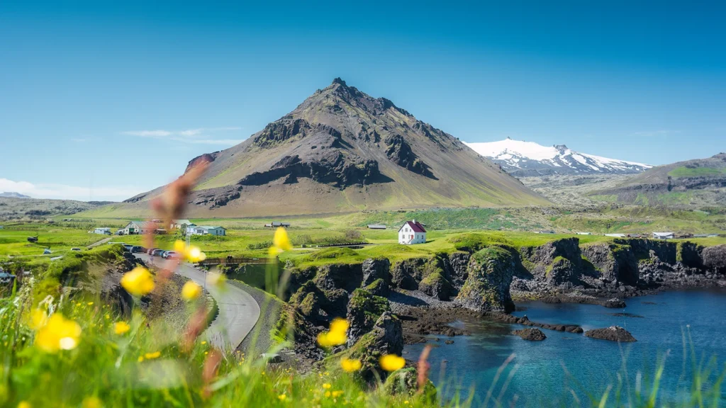 Arnarstapi en la península de Snaefellsnes: casa blanca sobre acantilados de lava y mar turquesa, con el Snaefellsjokull al fondo