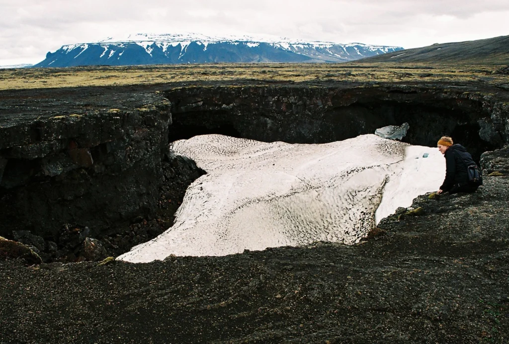 Entrada de la cueva de lava Surtshellir con nieve en el interior y paisaje volcánico en Islandia.