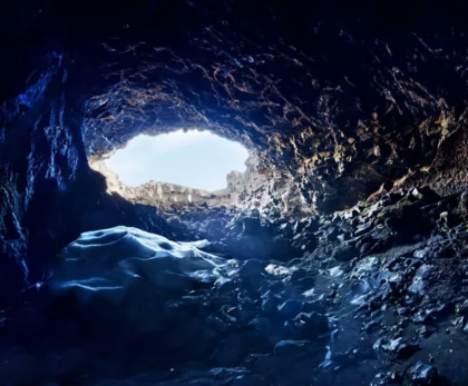 Interior oscuro de la cueva de lava Surtshellir con entrada de luz natural y hielo en Islandia.