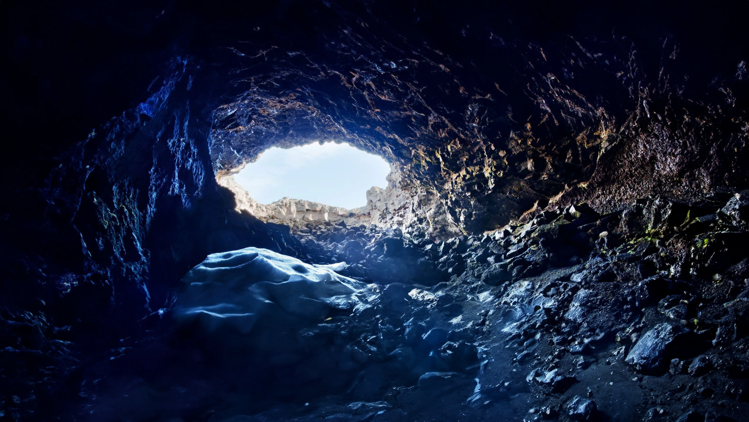 Interior oscuro de la cueva de lava Surtshellir con entrada de luz natural y hielo en Islandia.