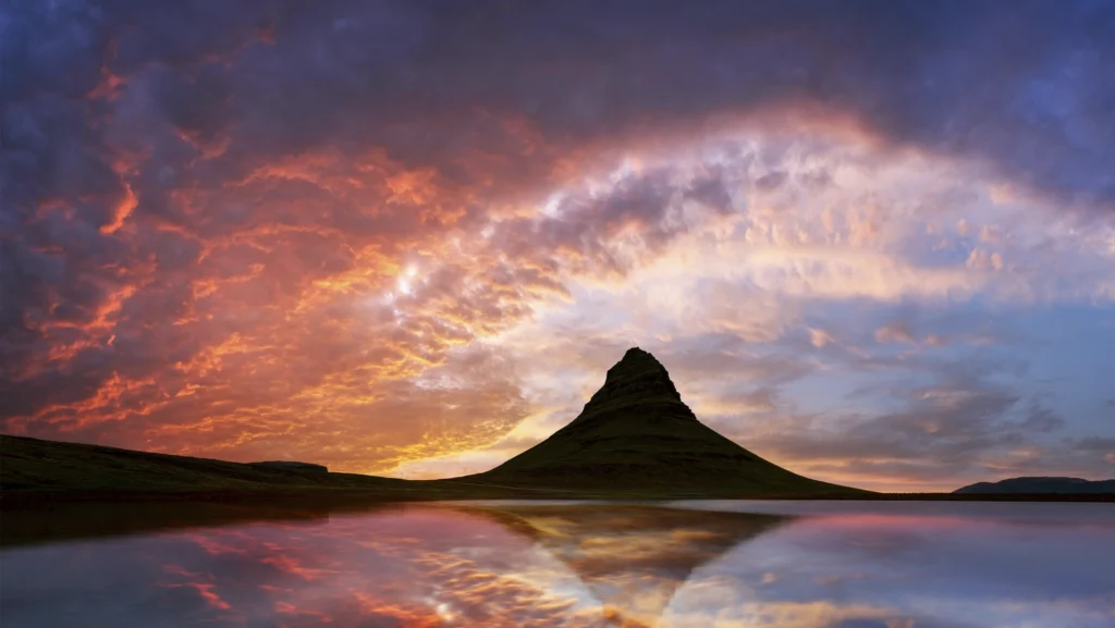 Monte Kirkjufell reflejado en el agua al atardecer con cielo dramático en Islandia.