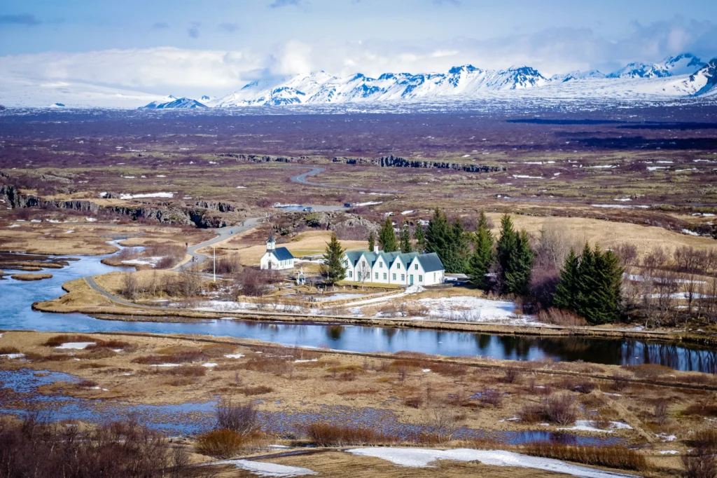 Vista panorámica del Parque Nacional Thingvellir con la iglesia Þingvallakirkja, el río Öxará y montañas nevadas al fondo en Islandia.