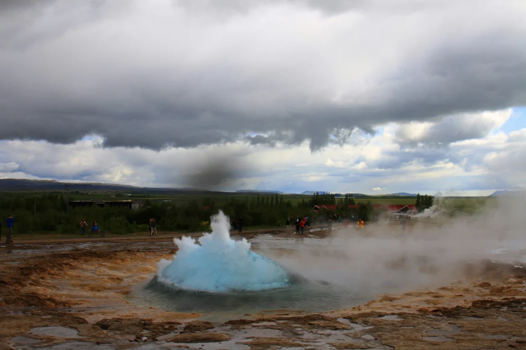 Burbuja azul del géiser Strokkur a punto de erupcionar con turistas al fondo