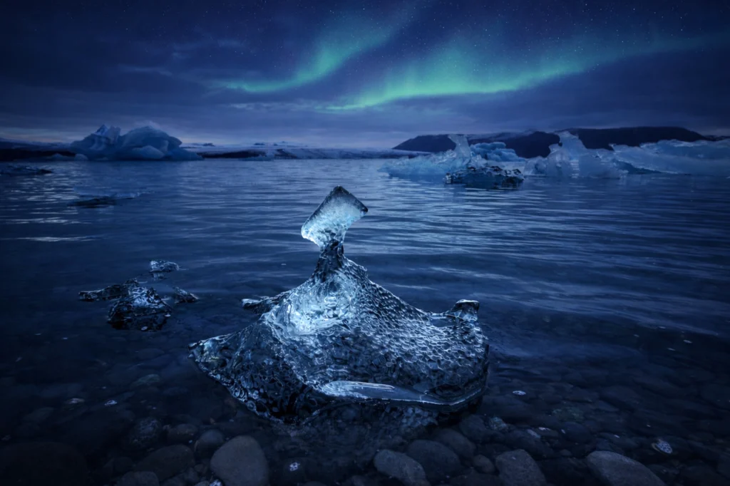 Aurora boreal sobre la laguna glaciar Jökulsárlón con iceberg en primer plano