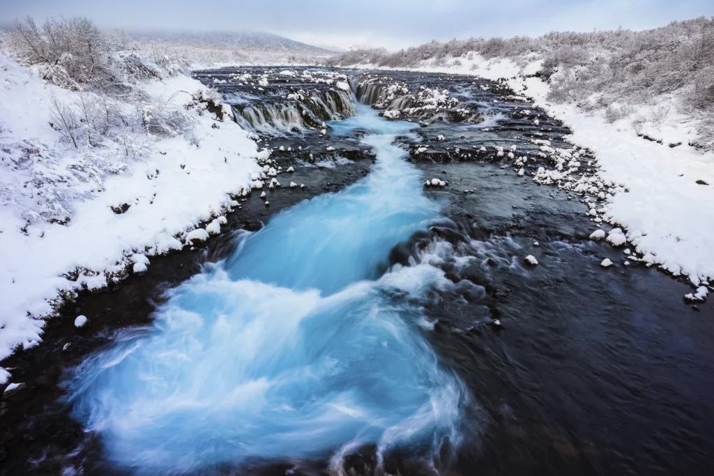 Cascada Bruarfoss en invierno con río azul turquesa y nieve en Islandia