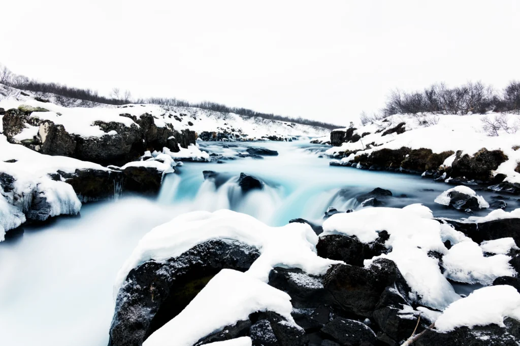 Cascada Bruarfoss en invierno con agua azul turquesa y rocas cubiertas de nieve en Islandia