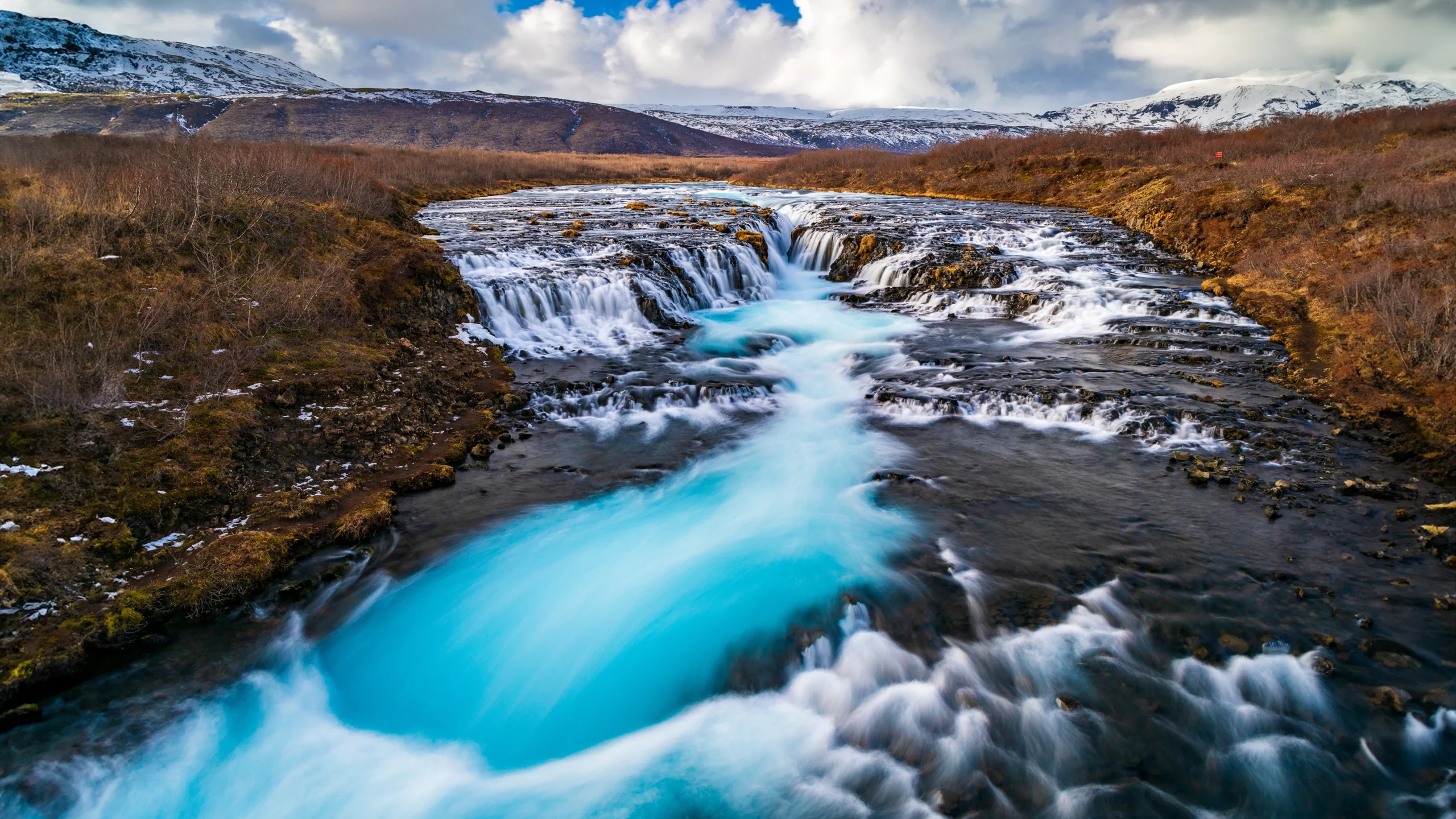 Cascada Bruarfoss con agua azul turquesa y paisaje montañoso en Islandia