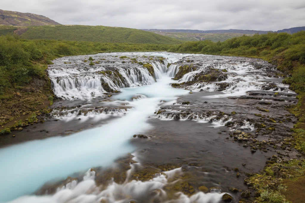 Cascada Bruarfoss con agua azul turquesa en paisaje verde de Islandia