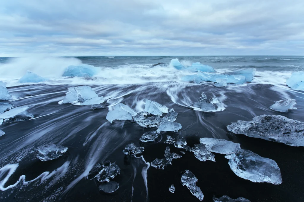 Bloques de hielo sobre la playa negra Diamond Beach con olas en Islandia