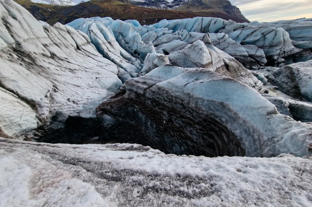 Grieta profunda en el glaciar Vatnajökull con hielo azul, capas de ceniza volcánica y texturas erosionadas