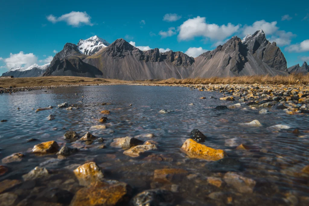 Río con piedras en primer plano y montaña Vestrahorn al fondo en Stokksnes Islandia