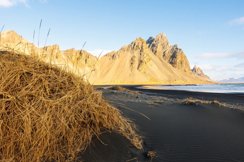 Dunas de arena negra en Stokksnes con la montaña Vestrahorn iluminada por el sol en Islandia