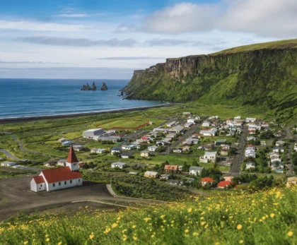 Vista panorámica de Borgarfjörður Eystri con iglesia roja, acantilados verdes y costa del este de Islandia