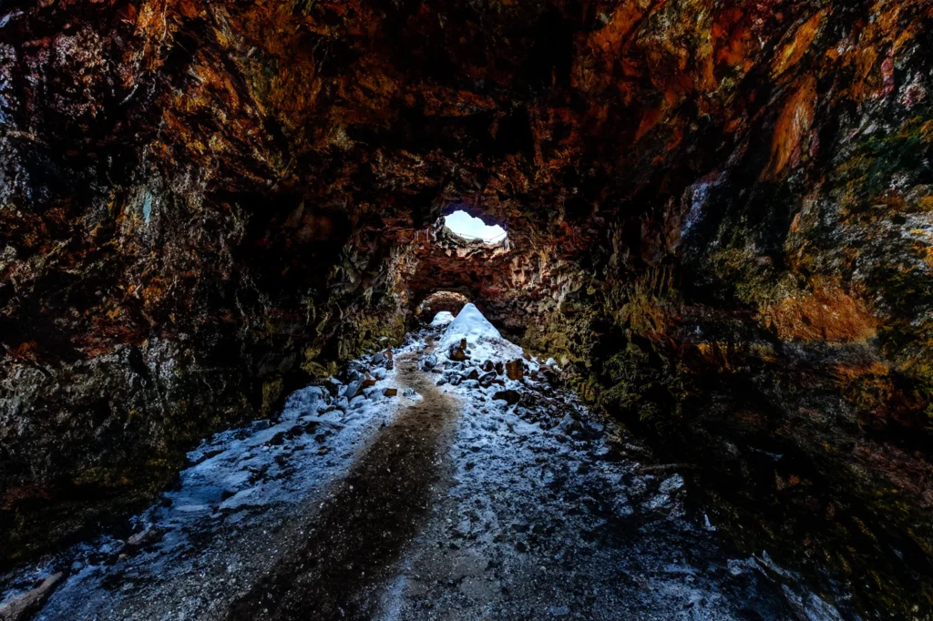 Interior de la cueva de lava Raufarhólshellir con entrada de luz natural y nieve
