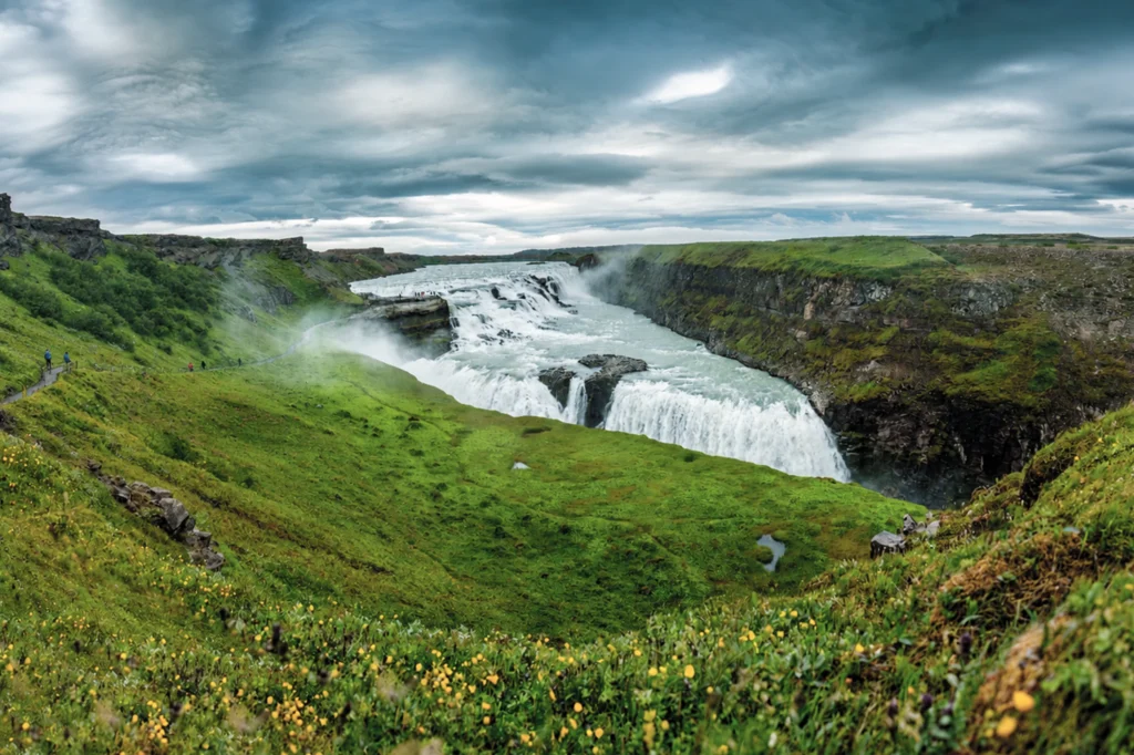 Cascada Gullfoss rodeada de paisaje verde en verano bajo cielo nublado en Islandia