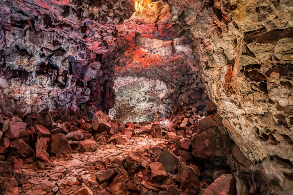 Interior de la cueva de lava Raufarhólshellir con formaciones rocosas rojizas y luz natural en Islandia