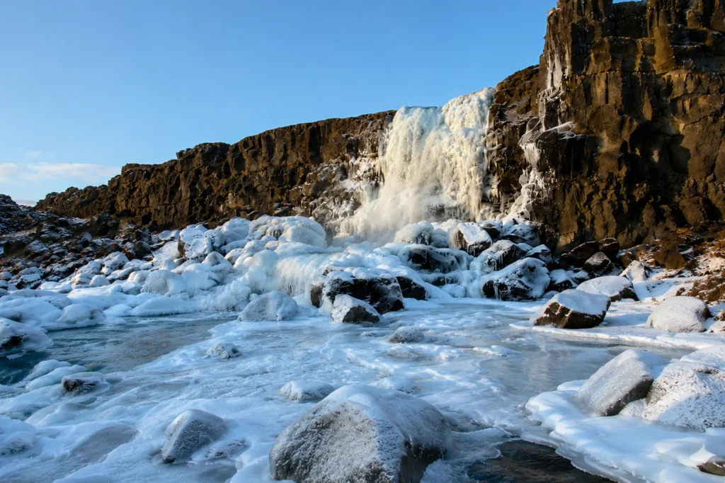 Cascada Öxarárfoss en invierno con hielo y nieve bajo cielo despejado en Thingvellir Islandia