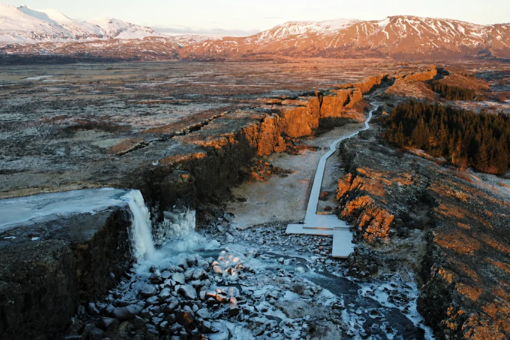 Vista aérea de la cascada Öxarárfoss al atardecer en Thingvellir con pasarela y paisaje volcánico