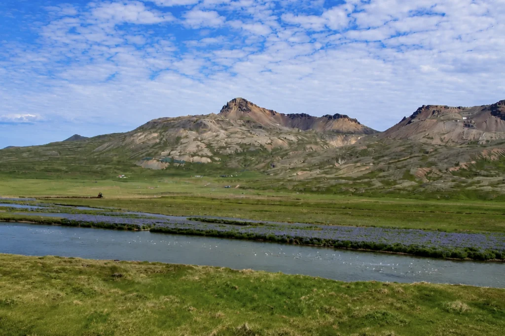 Paisaje de Borgarfjörður Eystri con río, praderas verdes y montañas volcánicas bajo cielo nublado en Islandia
