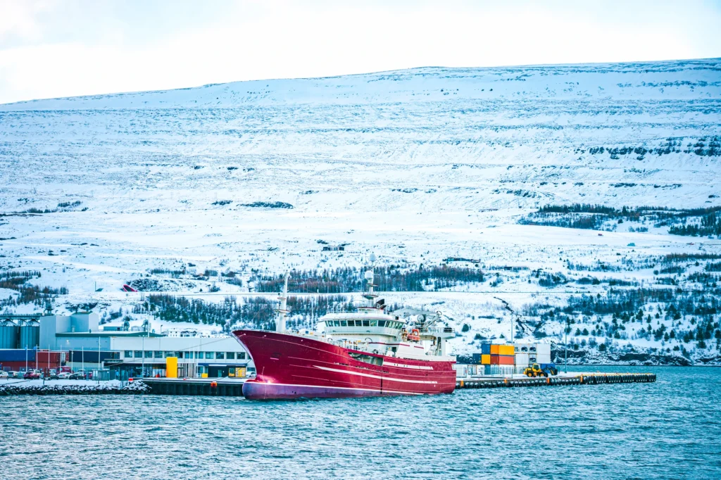 Barco pesquero rojo en el puerto de Akureyri con paisaje nevado en Islandia