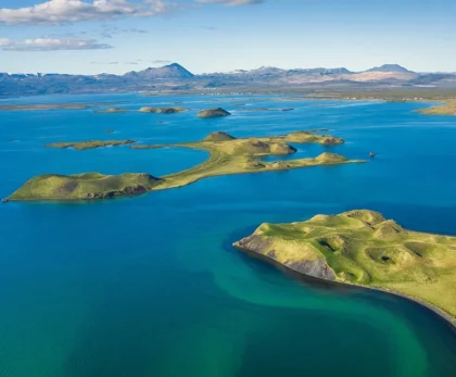 Lago Mývatn en Islandia con formaciones volcánicas, islotes verdes y aguas azules rodeadas de montañas