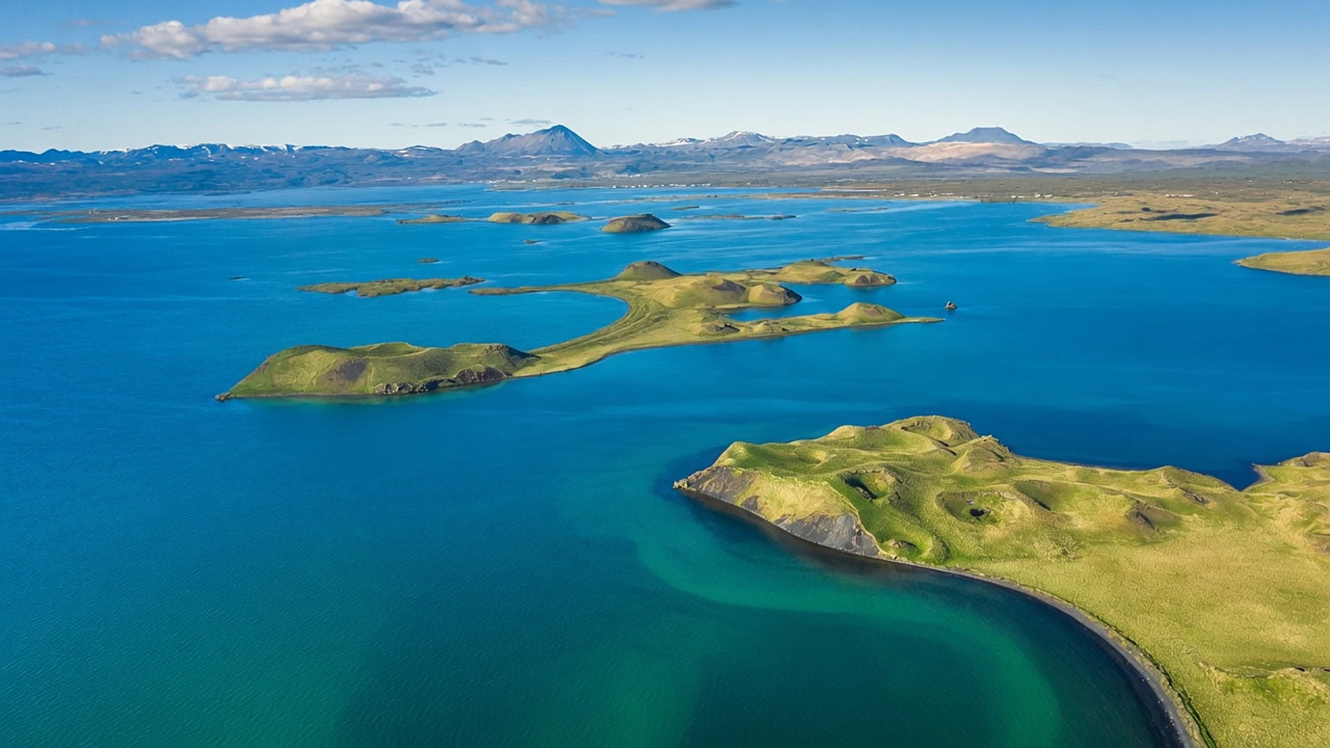 Lago Mývatn en Islandia con formaciones volcánicas, islotes verdes y aguas azules rodeadas de montañas