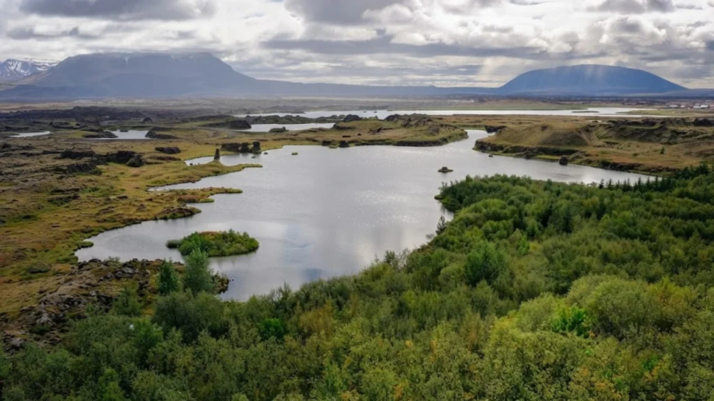 Lago Mývatn rodeado de vegetación y formaciones volcánicas con montañas al fondo en Islandia