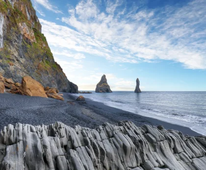 Playa de Reynisfjara con arena negra, columnas de basalto y formaciones rocosas en el mar en Islandia