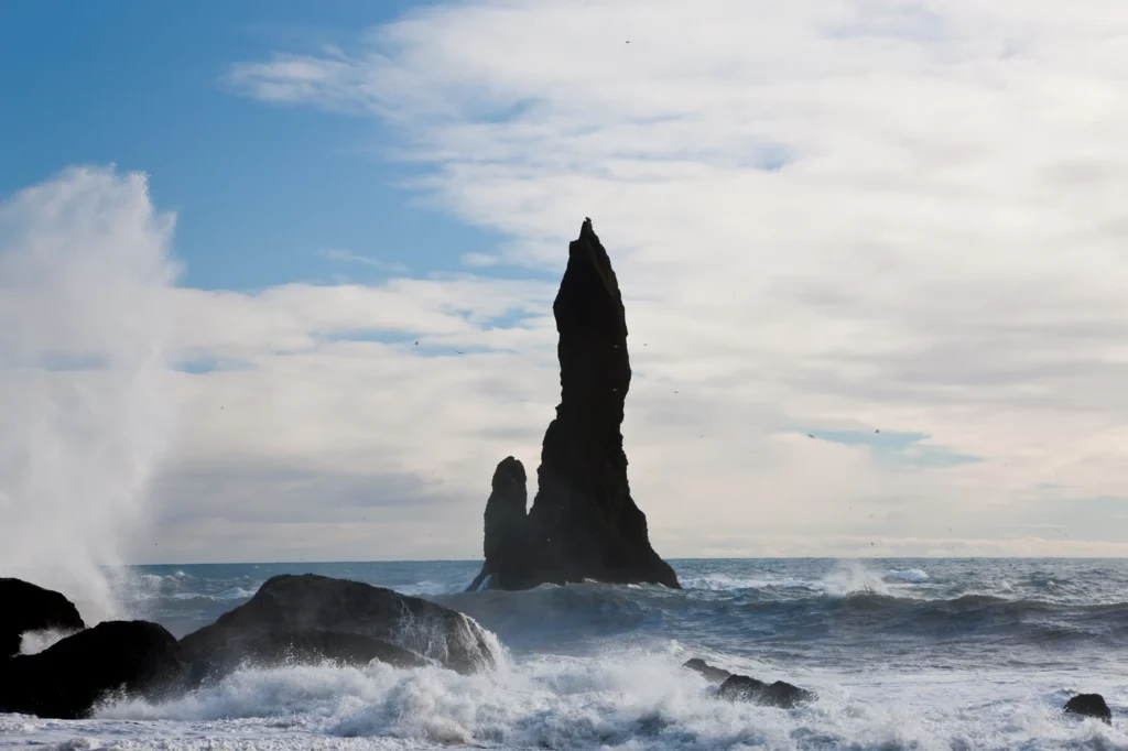 Farallón Reynisdrangar en Reynisfjara con olas rompiendo y aves sobrevolando la costa