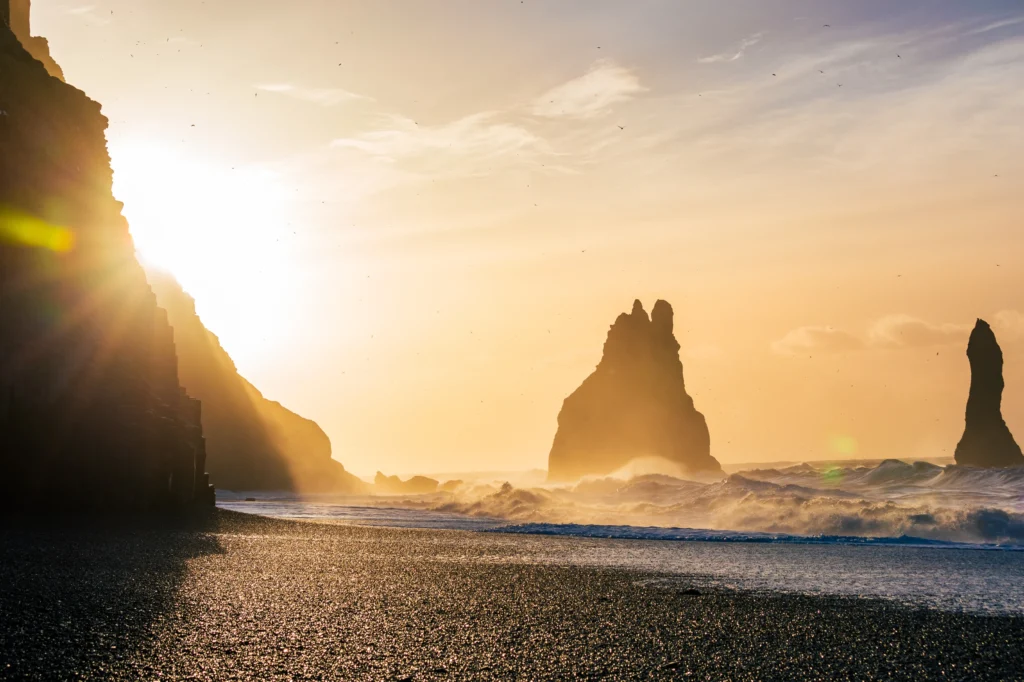 Atardecer en Reynisfjara con los farallones Reynisdrangar y olas iluminadas por el sol en Islandia