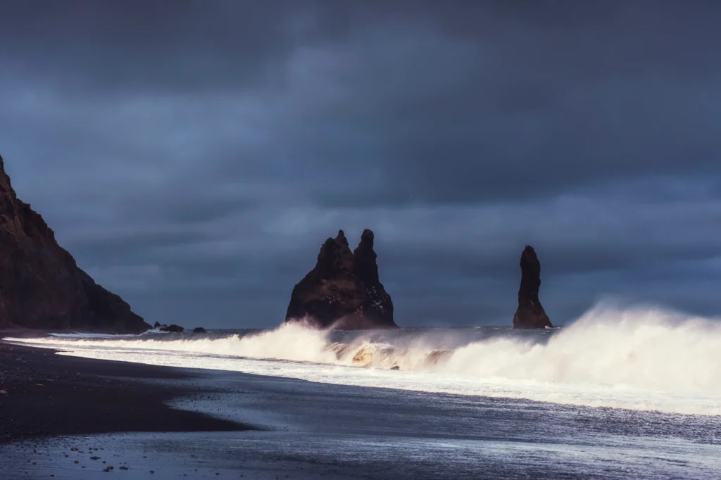 Olas rompiendo en la playa de Reynisfjara con los farallones Reynisdrangar bajo cielo nublado