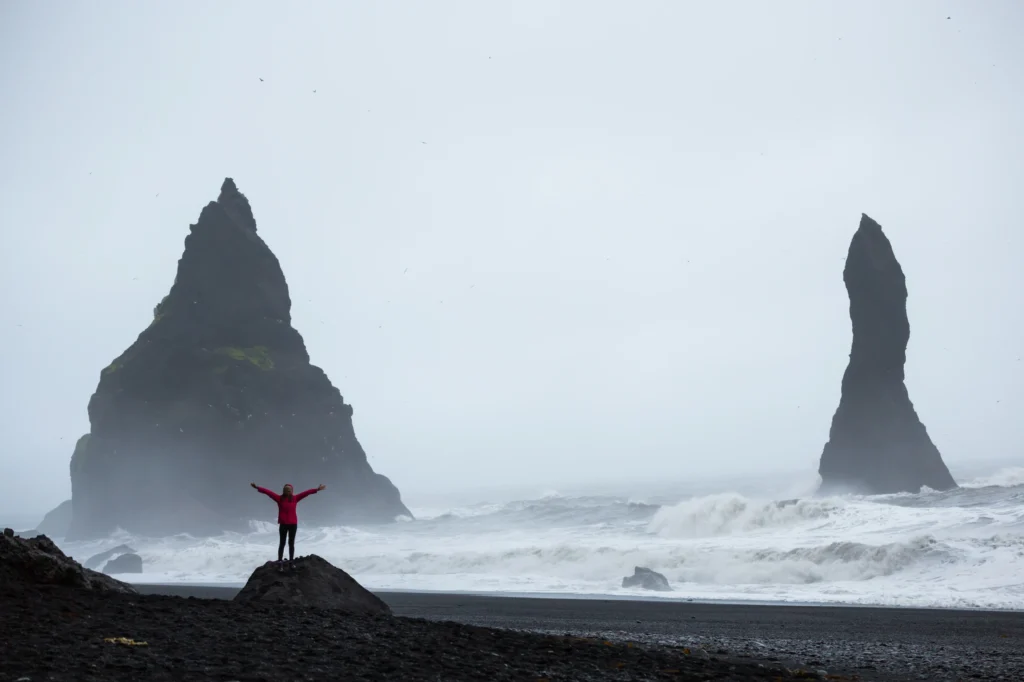 Persona en la playa de Reynisfjara frente a los farallones Reynisdrangar con mar embravecido en Islandia