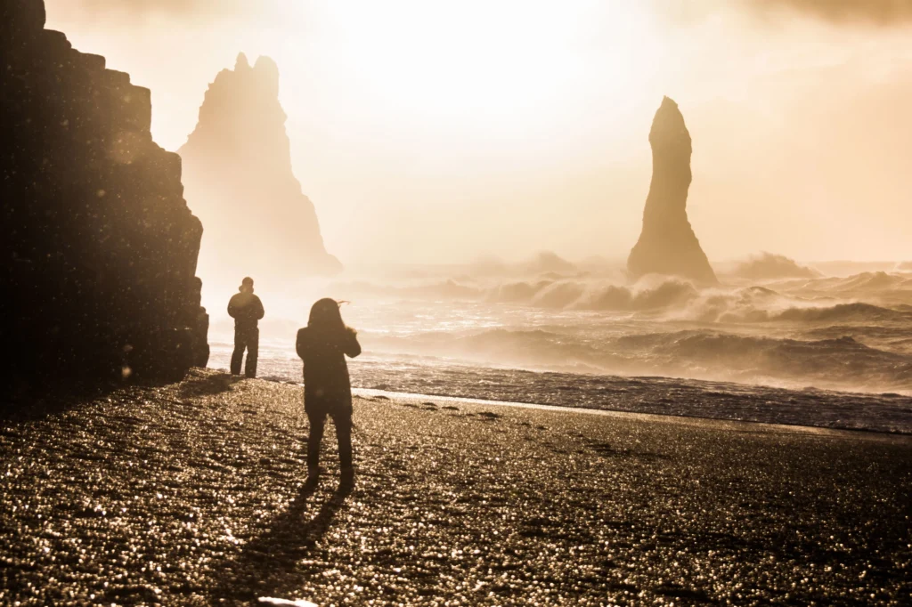 Personas en la playa de Reynisfjara al atardecer con farallones Reynisdrangar y olas del Atlántico