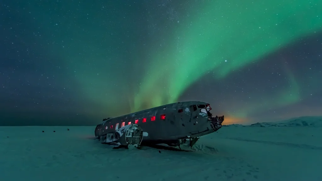 Avión de Sólheimasandur con auroras boreales sobre nieve en Islandia
