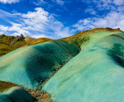 Primer plano de colinas turquesas y verdes en Grænihryggur, Islandia, bajo un cielo azul con nubes.