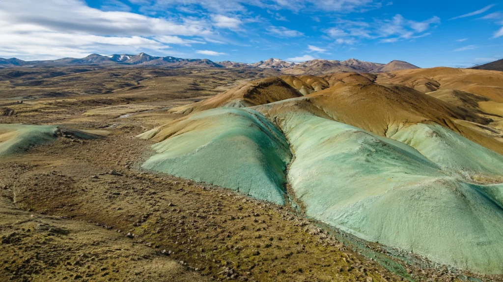 Montañas de tonos verdes y ocres en Grænihryggur, Islandia, bajo un cielo azul.