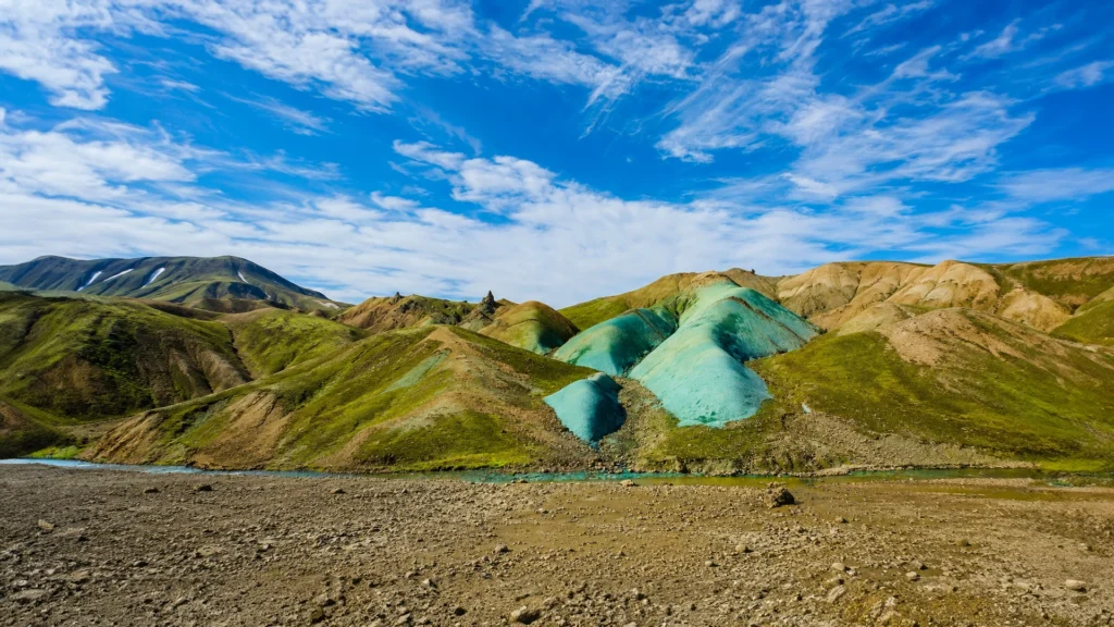 Vista panorámica de colinas turquesas y verdes en Grænihryggur, Islandia, bajo un cielo azul con nubes.