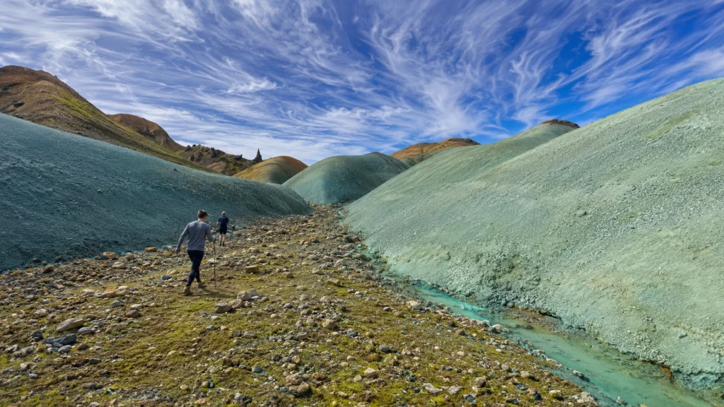 Dos senderistas recorren un valle entre colinas verdes de Grænihryggur, en Islandia.