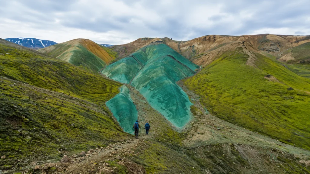 Dos senderistas avanzan entre colinas turquesas y verdes de Grænihryggur, en Islandia.