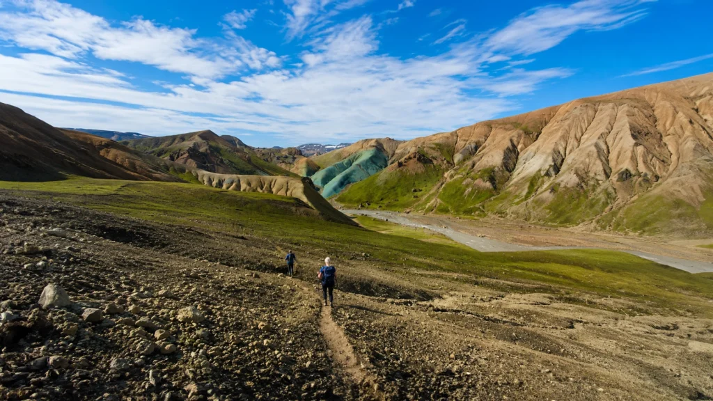 Dos senderistas descienden por un sendero entre montañas de colores en Grænihryggur, Islandia.