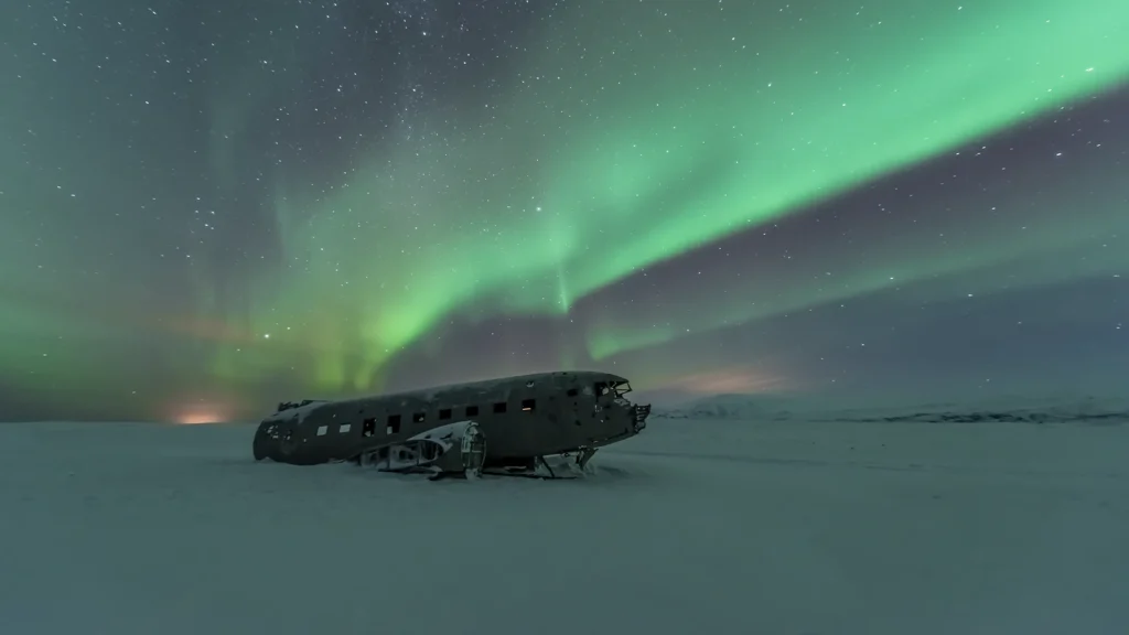 Aurora boreal verde sobre los restos de un avión abandonado en un paisaje nevado de Islandia