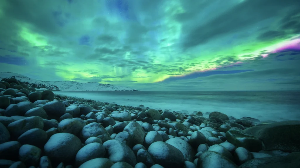 Aurora boreal verde y violeta sobre una costa rocosa junto al mar en Islandia