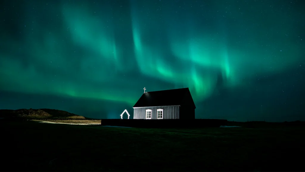 Aurora boreal verde sobre una iglesia negra bajo el cielo nocturno de Islandia